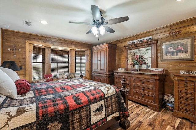 bedroom featuring light wood-type flooring, visible vents, wood walls, and a ceiling fan