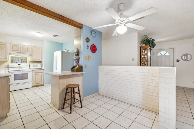 kitchen with a breakfast bar area, a textured ceiling, light tile patterned floors, and white appliances