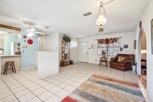 tiled living room with decorative columns, a textured ceiling, and ceiling fan