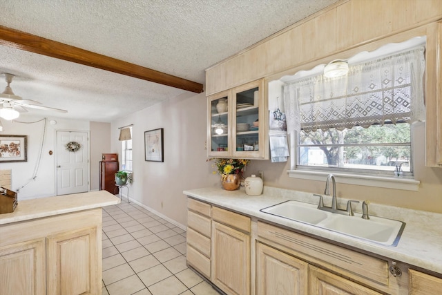 kitchen featuring light brown cabinets, beamed ceiling, sink, light tile patterned floors, and a textured ceiling