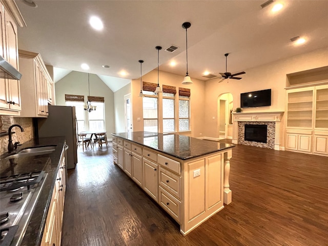 kitchen featuring sink, ceiling fan with notable chandelier, a kitchen island, a stone fireplace, and hanging light fixtures