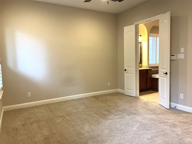 unfurnished bedroom with ensuite bath, light carpet, and ceiling fan