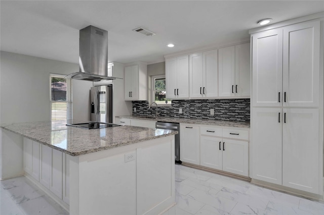 kitchen featuring tasteful backsplash, island range hood, stainless steel appliances, white cabinets, and light stone counters