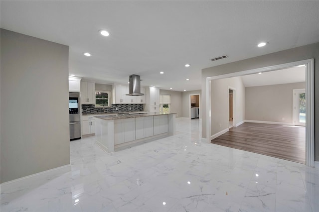 kitchen featuring wall chimney range hood, white cabinets, light hardwood / wood-style floors, and backsplash