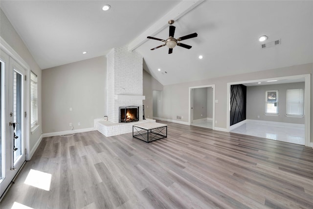 unfurnished living room with beam ceiling, light hardwood / wood-style flooring, a brick fireplace, high vaulted ceiling, and ceiling fan