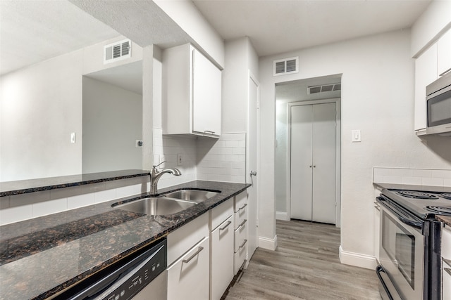 kitchen featuring decorative backsplash, stainless steel appliances, dark stone countertops, light wood-type flooring, and white cabinets