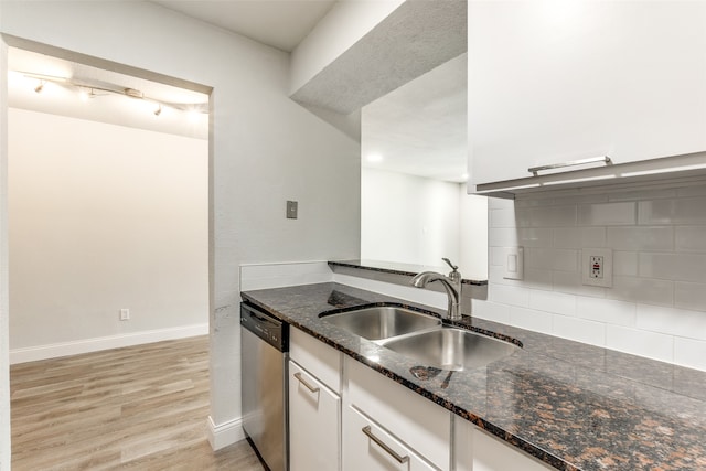 kitchen with white cabinetry, stainless steel dishwasher, dark stone countertops, light hardwood / wood-style floors, and sink