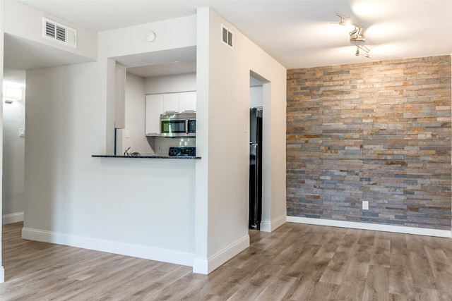 kitchen with light hardwood / wood-style floors, kitchen peninsula, white cabinets, and black fridge