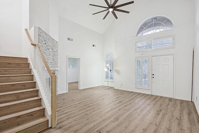 foyer with ceiling fan, a towering ceiling, and light wood-type flooring