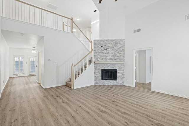 unfurnished living room with ceiling fan, a towering ceiling, light hardwood / wood-style flooring, and a fireplace