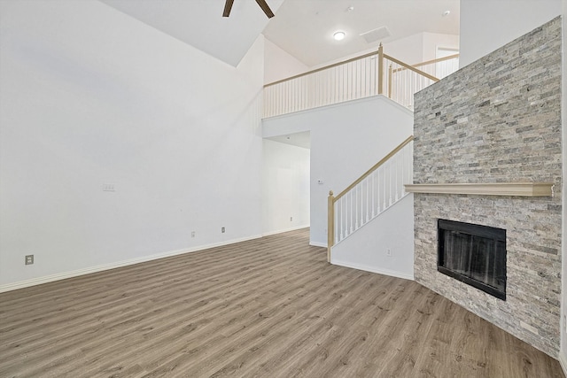 unfurnished living room featuring ceiling fan, high vaulted ceiling, a stone fireplace, and hardwood / wood-style floors