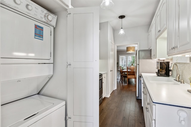 clothes washing area featuring sink, stacked washer and clothes dryer, and dark hardwood / wood-style flooring