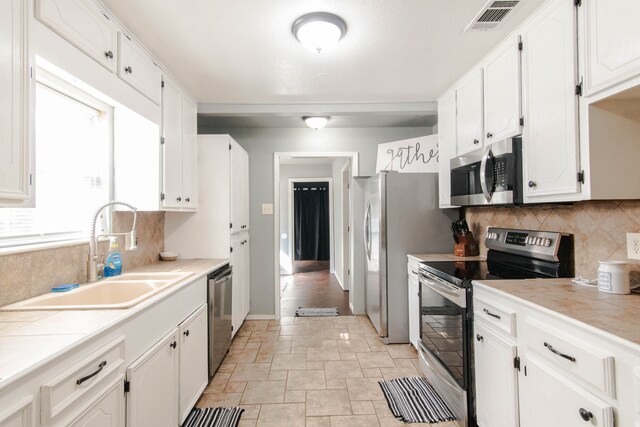 kitchen with appliances with stainless steel finishes, white cabinetry, a healthy amount of sunlight, and sink