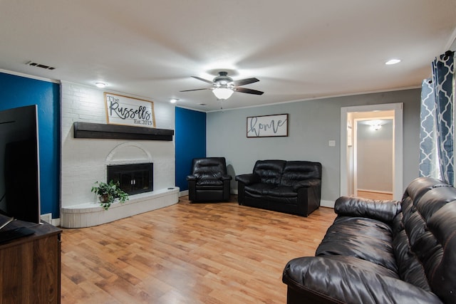 living room featuring ceiling fan, hardwood / wood-style flooring, ornamental molding, and a brick fireplace