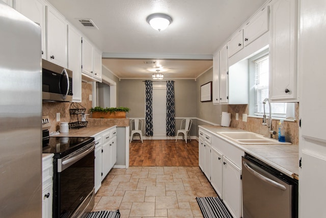 kitchen with tasteful backsplash, appliances with stainless steel finishes, sink, and white cabinets