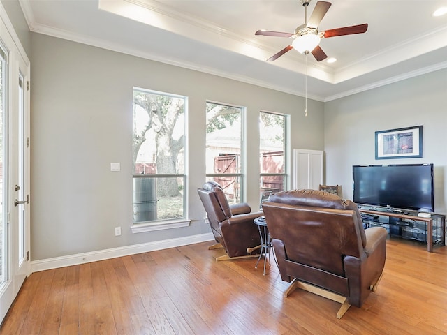 living room with light hardwood / wood-style floors, crown molding, a tray ceiling, and ceiling fan