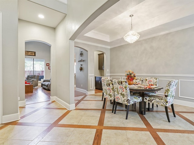 tiled dining area with a raised ceiling, ornamental molding, and a chandelier