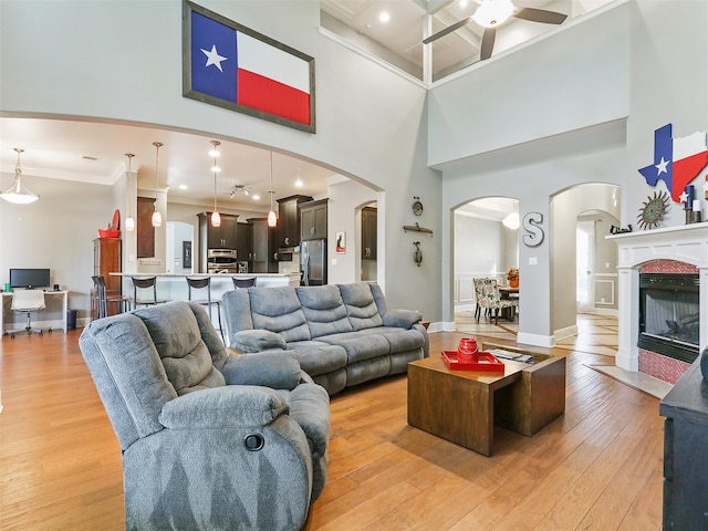 living room featuring a towering ceiling, ornamental molding, light wood-type flooring, and ceiling fan