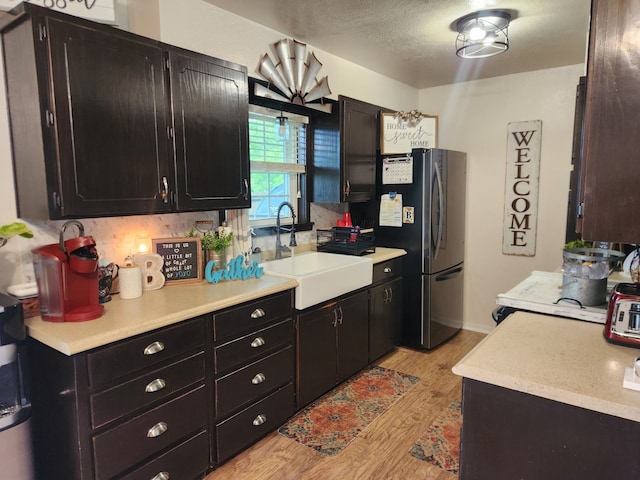 kitchen with sink, a textured ceiling, decorative backsplash, light hardwood / wood-style floors, and stainless steel refrigerator