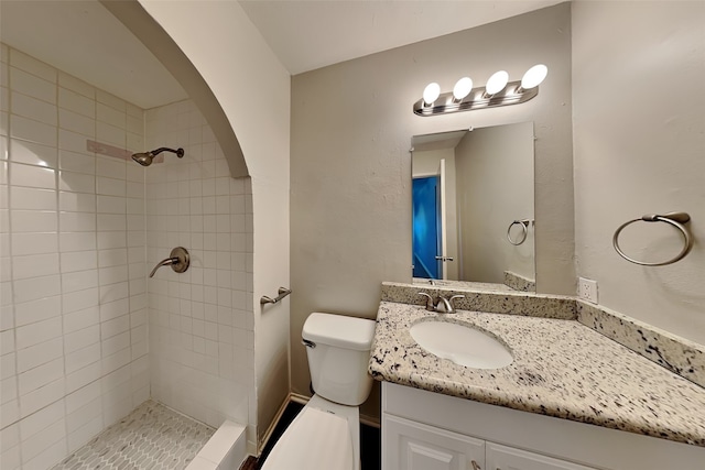 bathroom featuring a tile shower, vanity, and toilet