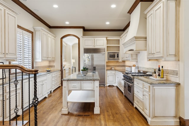 kitchen featuring a kitchen island, light stone countertops, custom range hood, and built in appliances