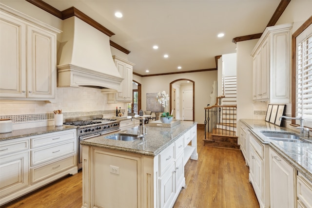 kitchen with a center island with sink, custom range hood, stainless steel stove, and sink