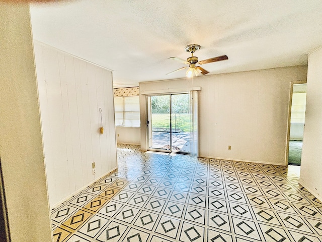 unfurnished room featuring wood walls, a textured ceiling, light tile patterned floors, and ceiling fan