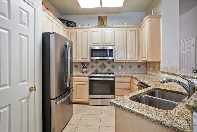 kitchen with decorative backsplash, sink, light stone countertops, light brown cabinetry, and appliances with stainless steel finishes