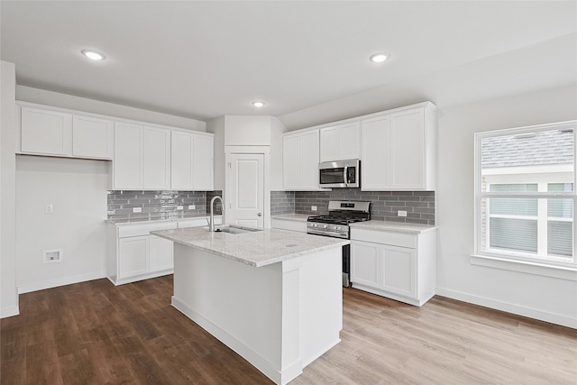 kitchen with sink, white cabinets, light stone counters, a center island with sink, and stainless steel appliances