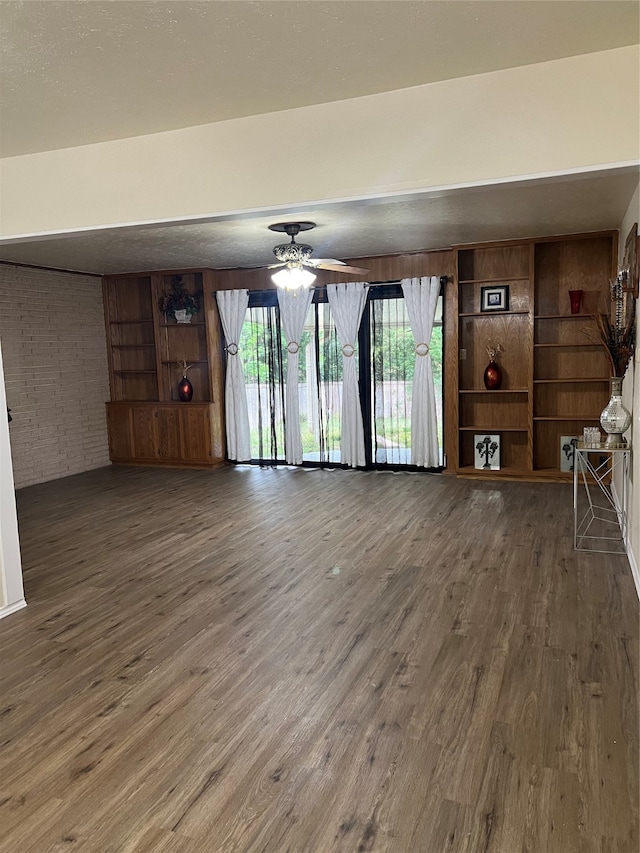 unfurnished living room with ceiling fan, brick wall, and dark hardwood / wood-style floors