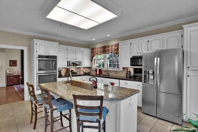 kitchen featuring light tile patterned floors, white cabinetry, stainless steel appliances, crown molding, and a center island