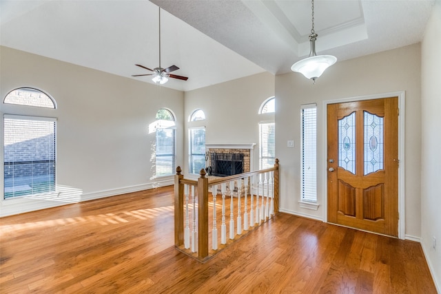 entryway featuring ceiling fan, wood-type flooring, a tray ceiling, and a brick fireplace