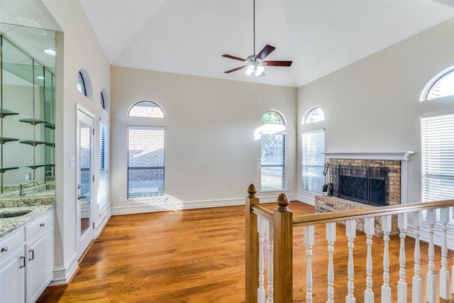 unfurnished living room featuring a brick fireplace, high vaulted ceiling, a healthy amount of sunlight, and light hardwood / wood-style floors