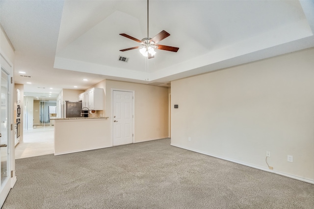 unfurnished living room with light carpet, a tray ceiling, and ceiling fan