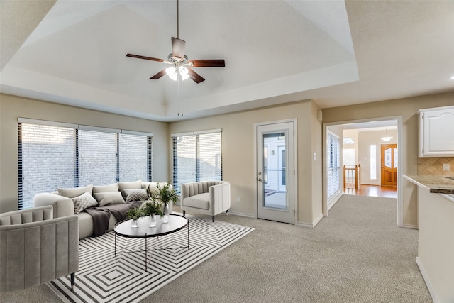 living room with a raised ceiling, a wealth of natural light, and light carpet