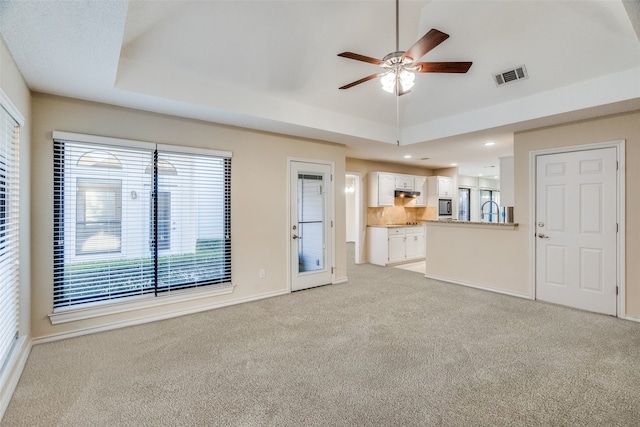 unfurnished living room with light carpet, a tray ceiling, and ceiling fan