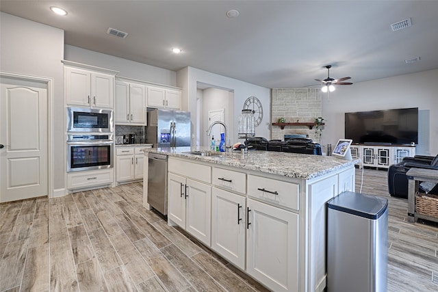 kitchen featuring light wood-type flooring, appliances with stainless steel finishes, a kitchen island with sink, and white cabinets