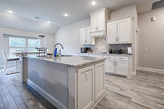 kitchen featuring sink, an island with sink, white cabinetry, light stone counters, and light hardwood / wood-style flooring