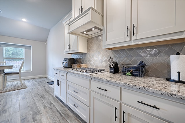 kitchen with custom exhaust hood, decorative backsplash, white cabinetry, stainless steel gas cooktop, and light hardwood / wood-style floors