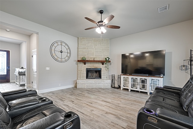 living room with a stone fireplace, wood-type flooring, and ceiling fan