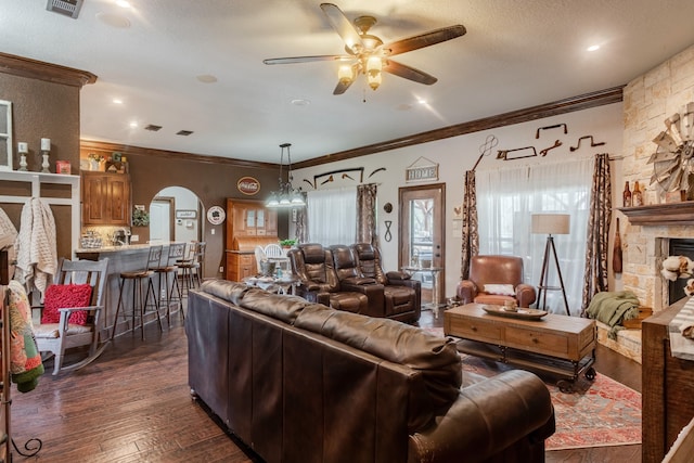 living room with a textured ceiling, dark hardwood / wood-style floors, ceiling fan with notable chandelier, a stone fireplace, and crown molding