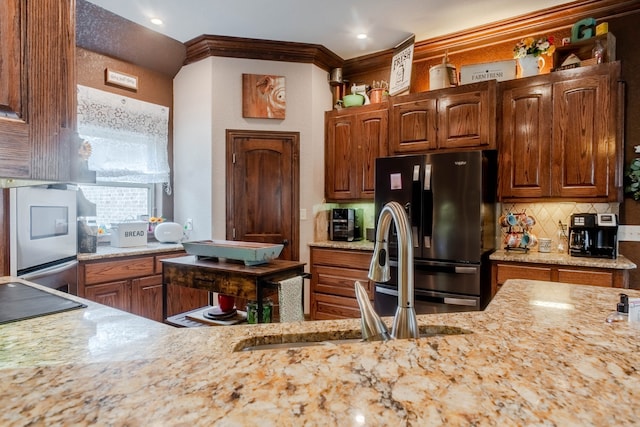 kitchen featuring sink, stainless steel fridge, light stone counters, and crown molding