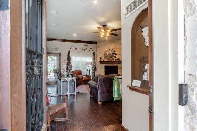 foyer featuring a stone fireplace, crown molding, ceiling fan, and dark hardwood / wood-style flooring