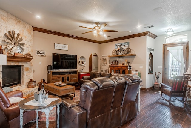 living room featuring a fireplace, a textured ceiling, ceiling fan, dark wood-type flooring, and ornamental molding