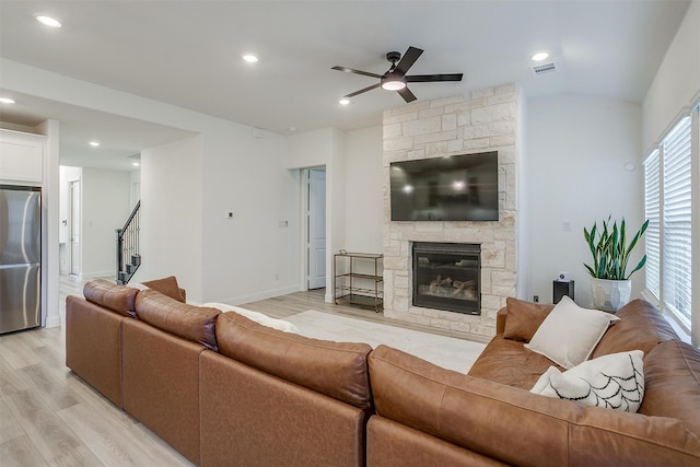 living room with a stone fireplace, light hardwood / wood-style flooring, and ceiling fan