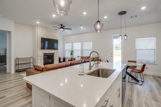 kitchen with sink, hanging light fixtures, light hardwood / wood-style floors, white cabinets, and a center island with sink