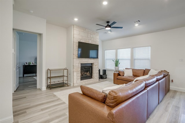 living room featuring a stone fireplace, light wood-type flooring, and ceiling fan