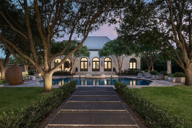 pool at dusk with a patio area and a lawn