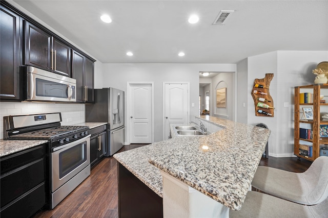 kitchen with a kitchen breakfast bar, a center island with sink, dark hardwood / wood-style floors, and appliances with stainless steel finishes