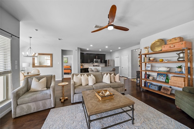 living room featuring ceiling fan with notable chandelier and dark wood-type flooring